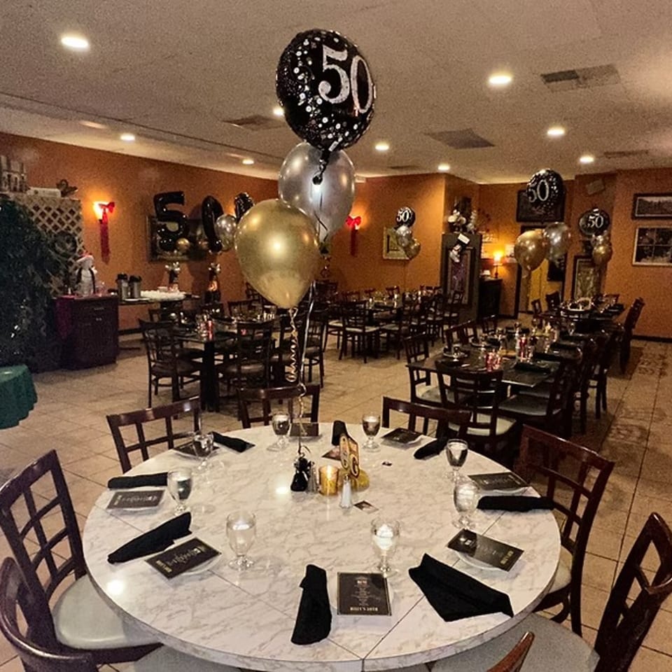 Restaurant dining room decorated with black, gold, and silver "50" balloons for a celebration.