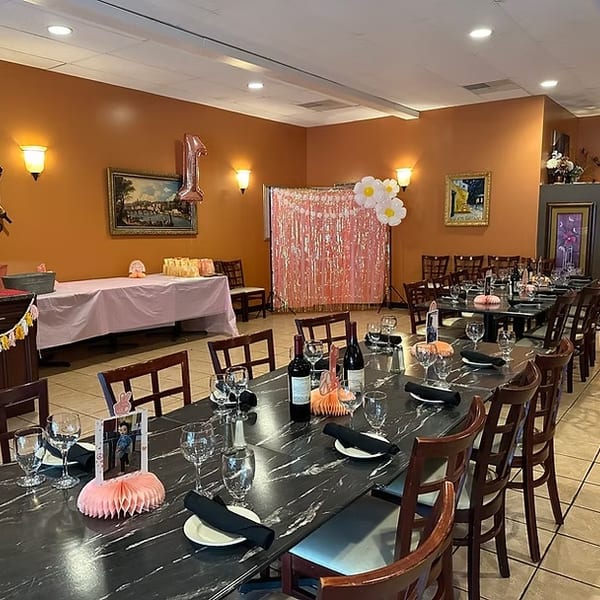 Restaurant dining room set up for a birthday party with long tables, decorations, and a pink backdrop.