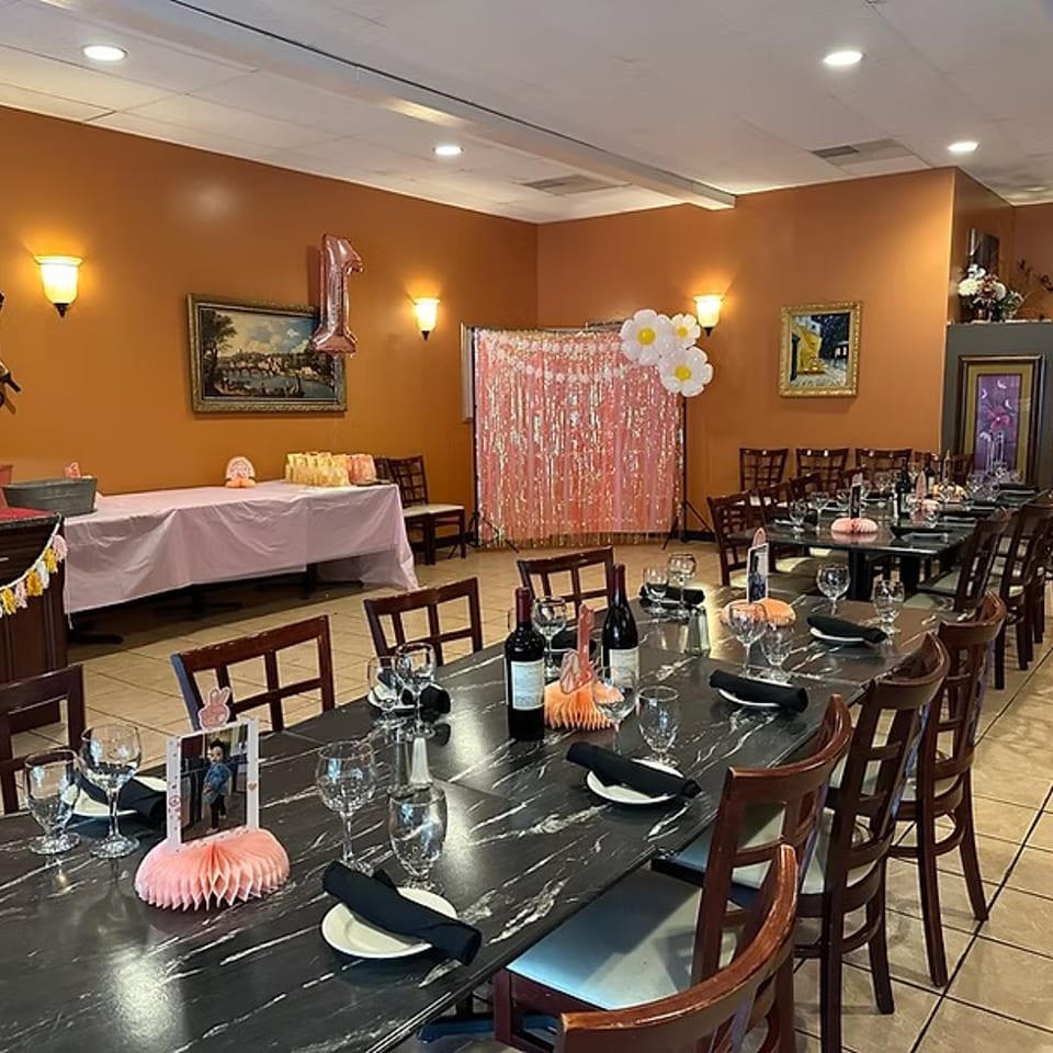 Restaurant dining room set up for a birthday party with long tables, decorations, and a pink backdrop.