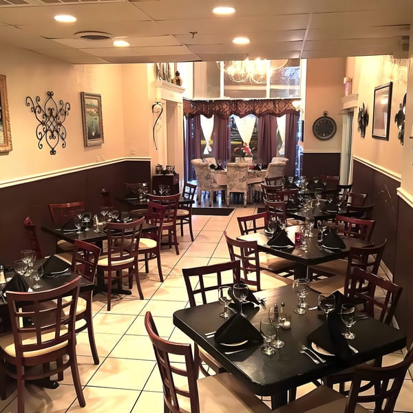 Empty restaurant dining room with dark tables, wooden chairs, and elegant decor.