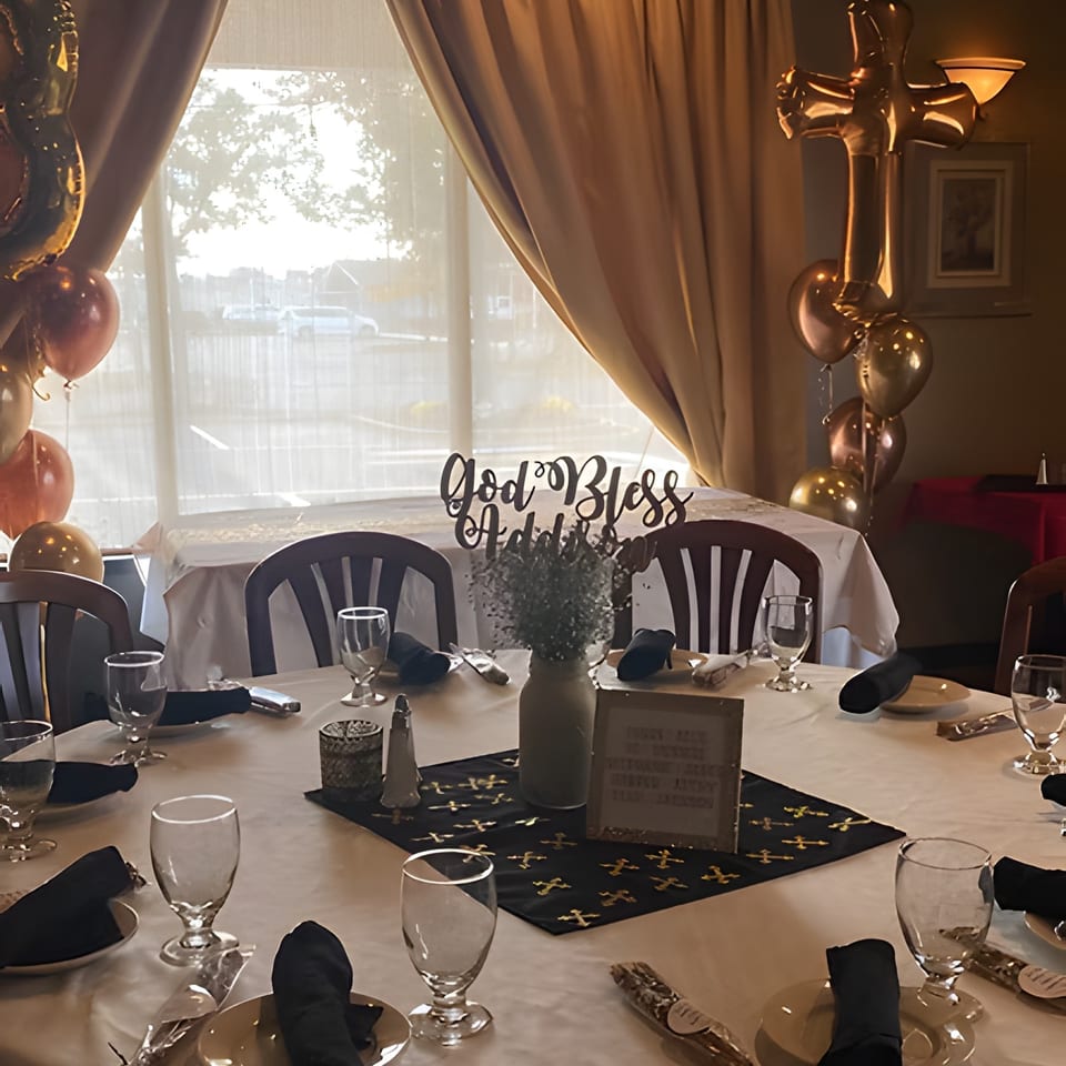 A decorated table with a "God Bless" sign, balloons, and place settings for a special event.