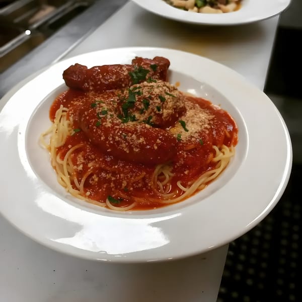 Spaghetti with meatballs and sausages, topped with red sauce, parmesan cheese, and parsley.