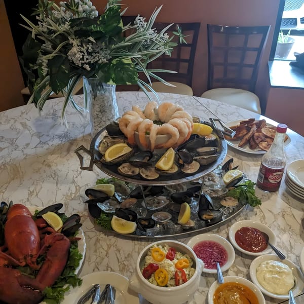 A lavish seafood tower with shrimp, oysters, mussels, clams, lobster, and various sauces on a marble table.