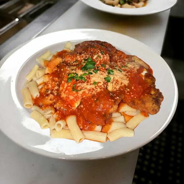 Chicken parmesan with rigatoni pasta, red sauce, and parsley on a white plate.